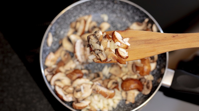 Wooden spatula holding mushrooms and onions over a pan