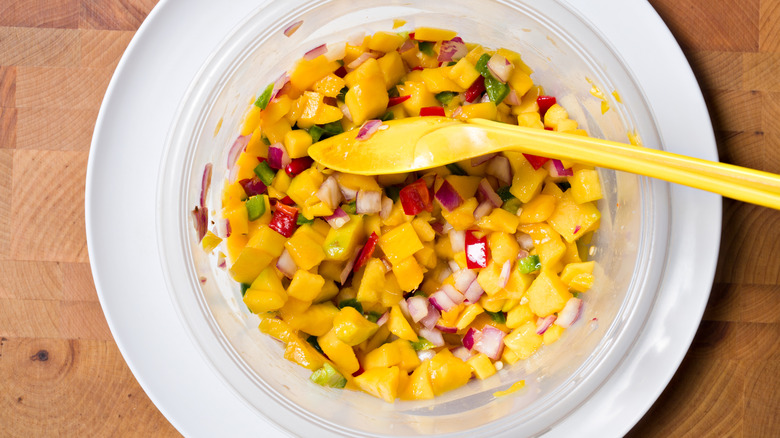 a bowl of fresh mango salsa with a yellow spoon sitting inside