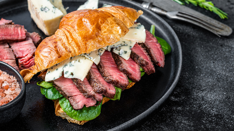 Sliced beef tenderloin in croissant sandwich with greens and blue cheese