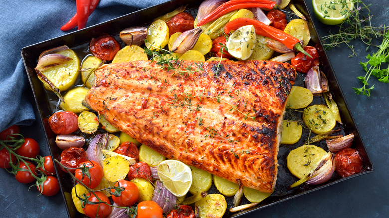 Baked salmon on a baking sheet with colorful vegetables.