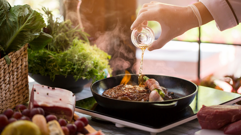A person pouring whiskey into a pan as they flambe steak