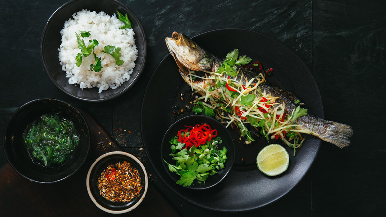 steamed whole fish alongside rice, seaweed salad, and herbs