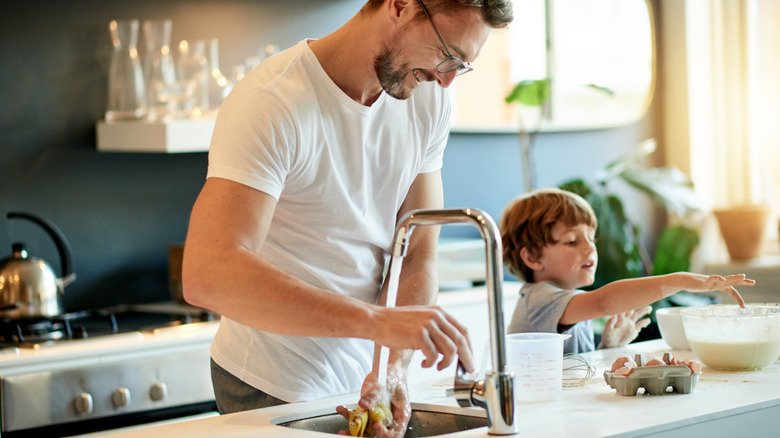 Man washing dishes near child with pancake batter