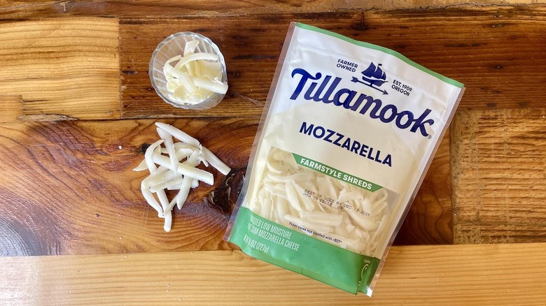 Overhead view of a bag and glass of Tillamook Farmstyle Part-Skim Shredded Mozzarella Cheese on a wooden table