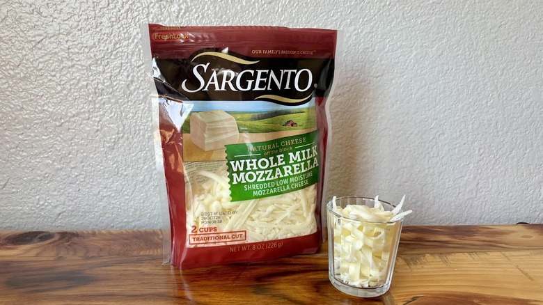 A bag and small glass of Sargento Whole Milk Shredded Mozzarella Cheese sitting on a wooden table