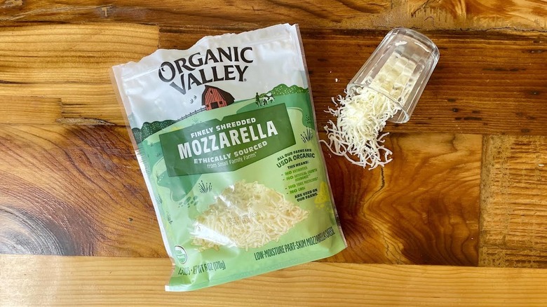 Overhead view of a bag and glass of Organic Valley Part-Skim Shredded Mozzarella Cheese on a wooden table