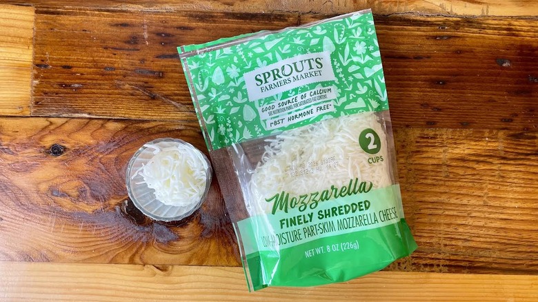 Overhead view of a glass and bag of Sprouts Part-Skim Shredded Mozzarella Cheese on a wooden table