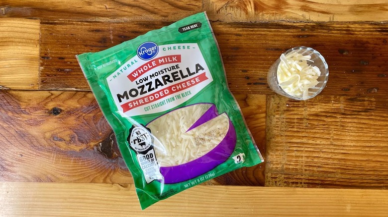 Overhead view of a bag and small glass of Kroger Whole Milk Shredded Mozzarella Cheese on a wooden table
