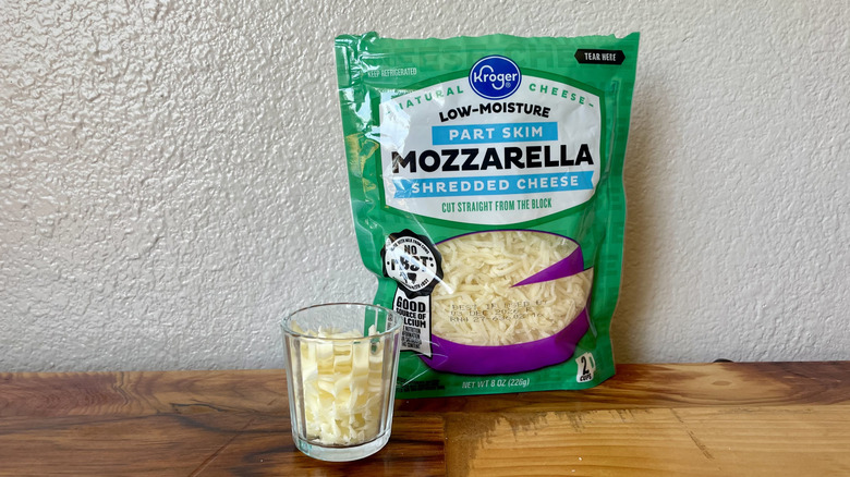 A bag and small glass of Kroger Part-Skim Shredded Mozzarella Cheese on a wooden table