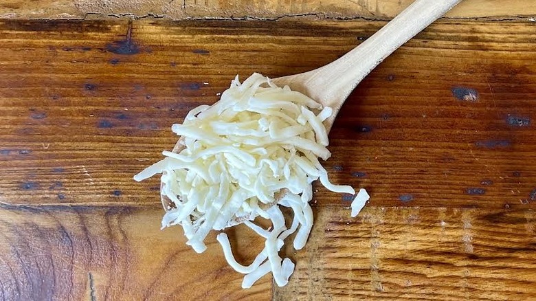 A large wooden spoon full of shredded mozzarella cheese lying on a wooden table top