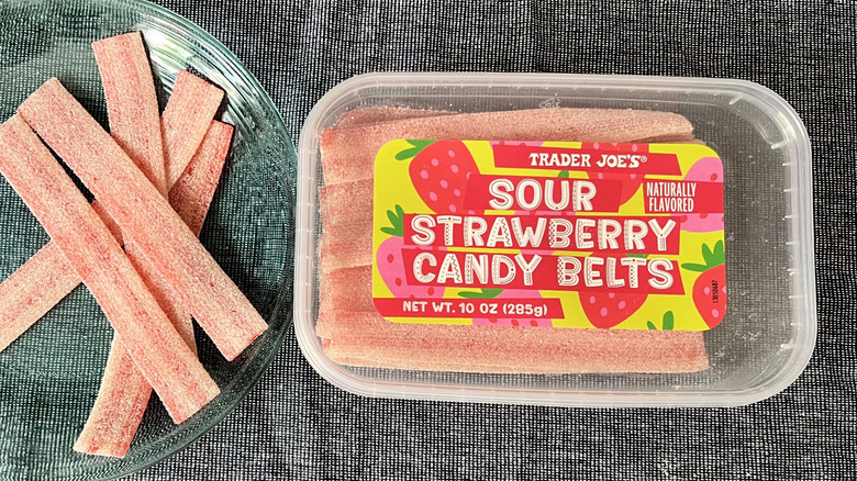 A handful of Trader Joe's Sour Strawberry Candy Belts on a glass plate next to a plastic box of Sour Strawberry Candy Belts