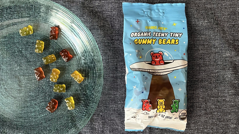 A handful of Trader Joe's Organic, Teeny Tiny Gummy Bears on a glass plate next to a bag of Teeny, Tiny Gummy Bears