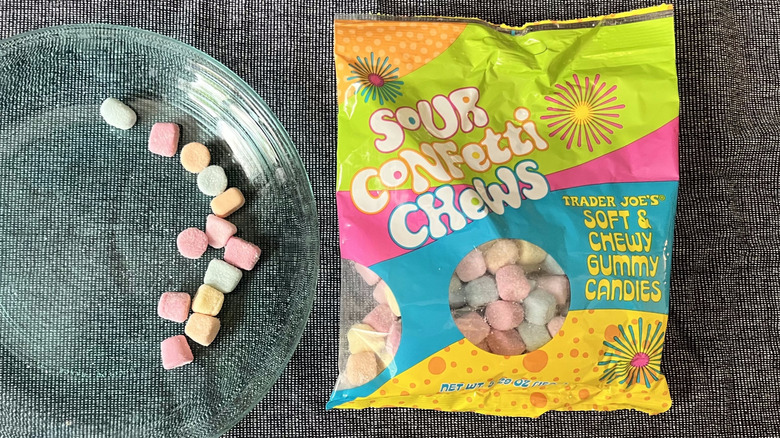 A handful of Trader Joe's Sour Confetti Chews on a glass plate next to a bag of Sour Confetti Chews