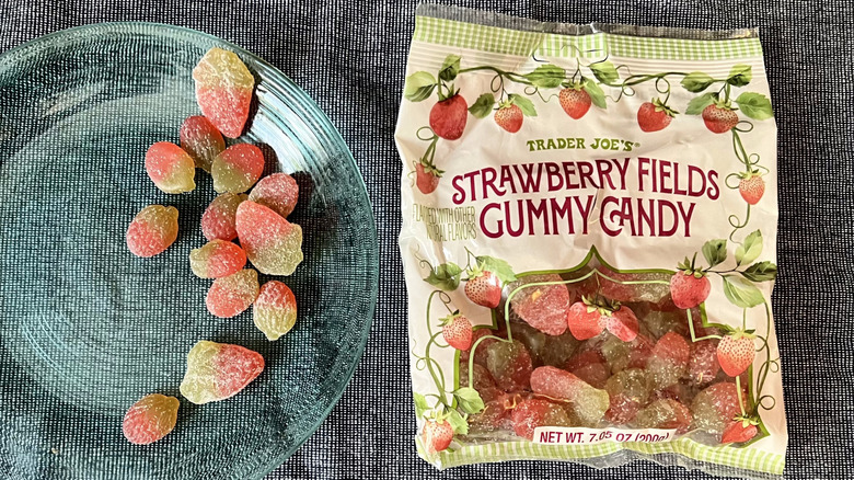 A handful of Trader Joe's Strawberry Fields Gummy Candy on a glass plate next to a bag of Strawberry Fields Gummy Candy