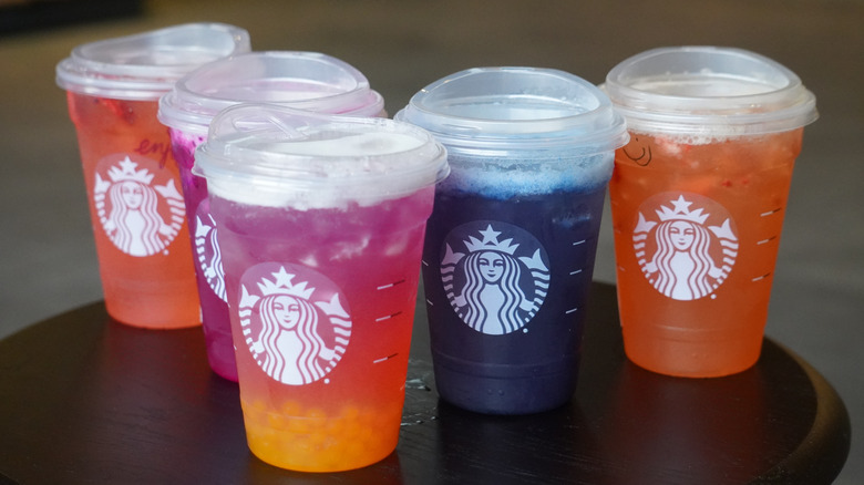 Side view of Starbucks' Strawberry Açaí Lemonade Refresher, Mango Dragonfruit Lemonade Refresher, Tropical Butterfly Lemonade Refresher, Blue Coconut Lemonade Refresher, and Mango Strawberry Lemonade Refresher (left to right).