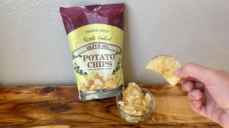 Hand holding a Kettle Cooked Olive Oil Potato Chip next to the bag
