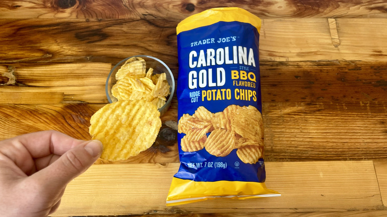 Hand holding a Carolina Gold Style BBQ Flavored Ridge Cut Potato Chip next to the bag