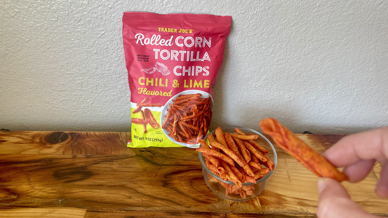 Hand holding a Chili & Lime Flavored Rolled Corn Tortilla Chip next to the bag