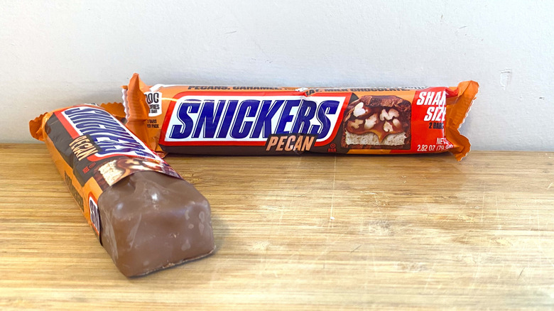 Wrapped Snickers Pecan bar with a partially wrapped Snickers Pecan bar on the left side