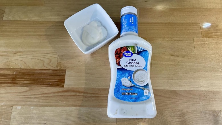 Overhead view of a bottle and ramekin of Great Value Blue Cheese Dressing on wooden countertop