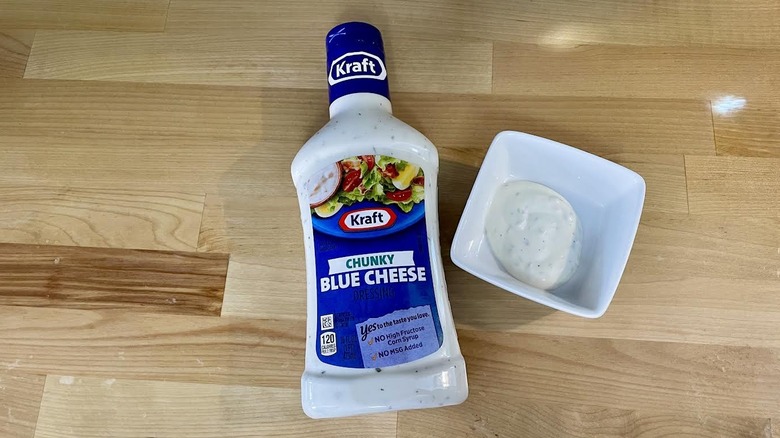 Overhead view of a bottle and ramekin of Kraft Chunky Blue Cheese Dressing on wooden countertop
