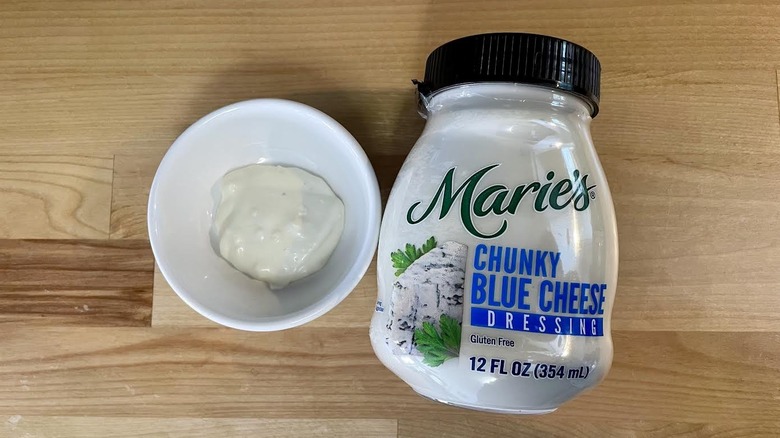 Overhead view of a bottle and ramekin of Marie's Real Premium Chunky Blue Cheese Dressing on wooden countertop