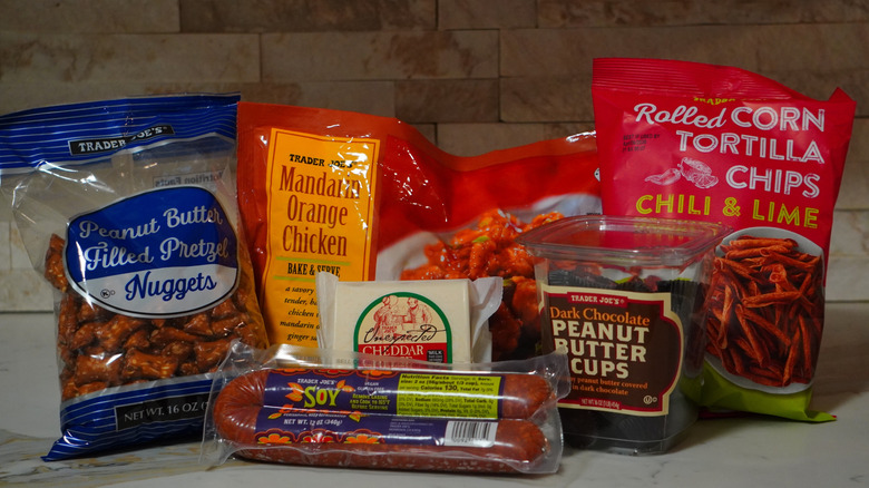 Trader Joe's Peanut Butter Filled Pretzel Nuggets, Soy Chorizo, Unexpected Cheddar Cheese, Mandarin Orange Chicken, Dark Chocolate Peanut Butter Cups, and Chili & Lime Rolled Corn Tortilla Chips arranged on countertop