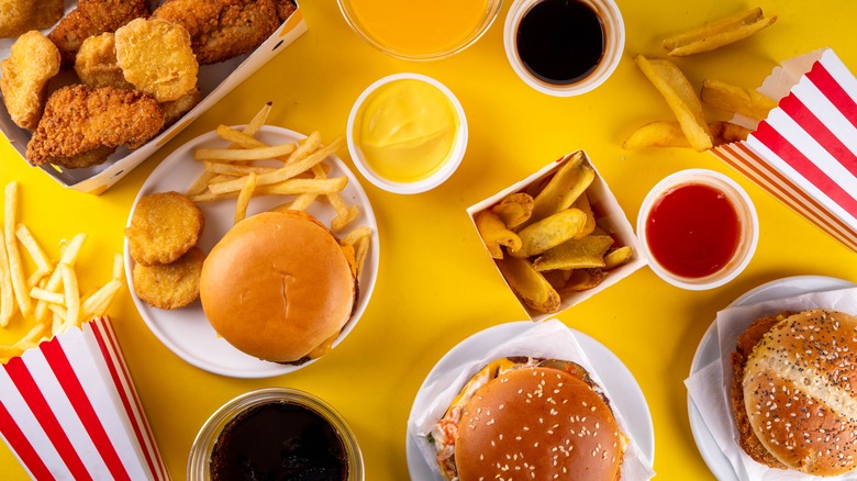 Multiple platters of fast food items, including burgers, nuggets, and fries, sit on a yellow background
