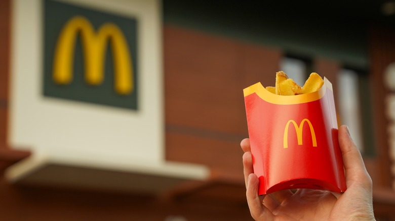 A hand holds McDonald's french fries outside a McDonald's restaurant