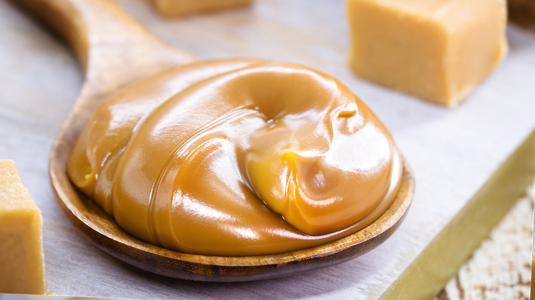 Spoonful of gooey dulche de leche next to homemade caramels
