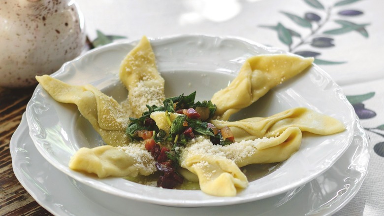 Cooked casoncelli in a bowl topped with pancetta and grated cheese 