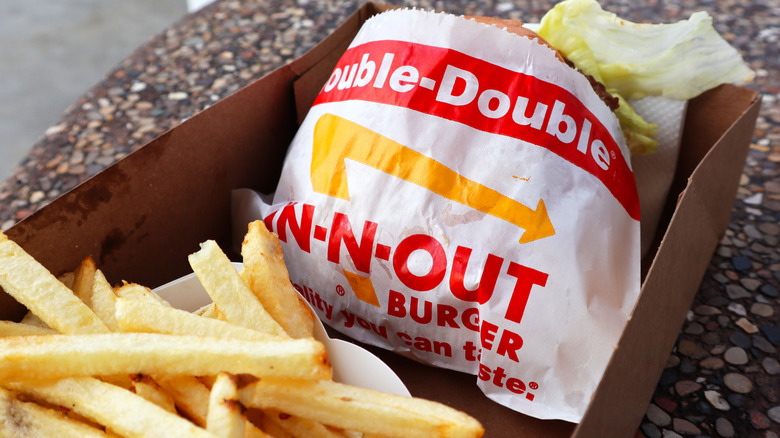 An In-N-Out Double-Double burger and french fries sit in a cardboard container on a restaurant counter