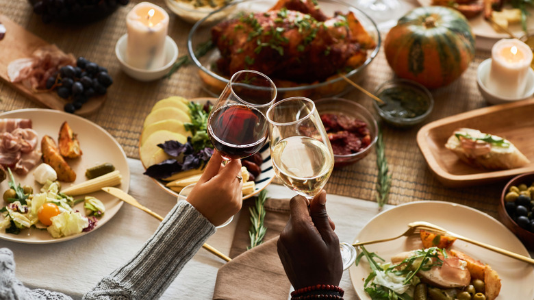 Two people clinking wine glasses at the Thanksgiving dinner table.
