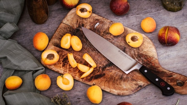 chef's knife on cutting board with sliced peaches