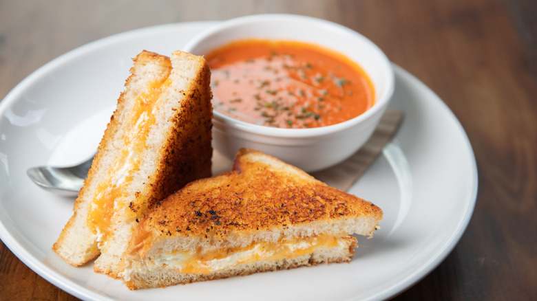Grilled cheese cut in half with bowl of tomato soup