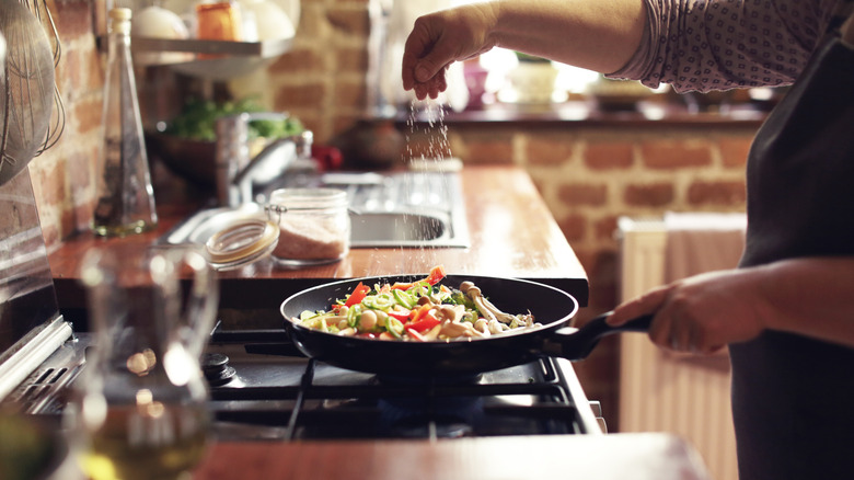 person seasoning roasted vegetables in kitchen