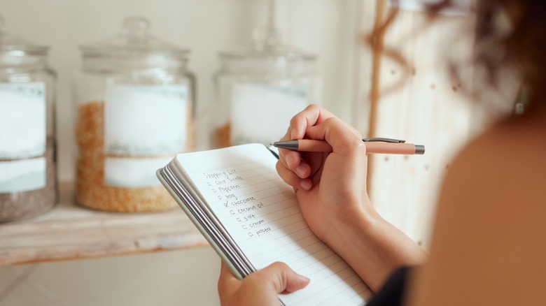 person writing a shopping list in their kitchen