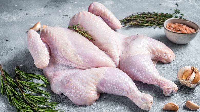 Raw spatchcocked chicken on cutting board with herbs