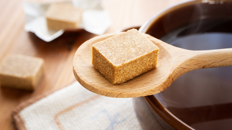 Bouillon cube on a wooden spoon next to a bowl of broth