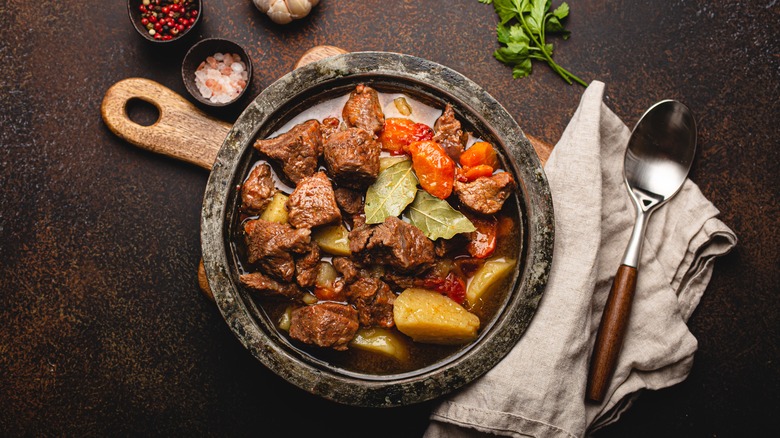 beef stew in a bowl with ramekins of herbs, a sprig of parsley, and a spoon on a napkin