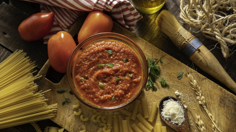 A bowl of sauce with spaghetti and tomatoes on the side