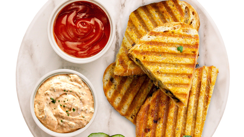 Grilled cheese sandwiches stacked next to a ramekin of ketchup and one of a spicy mayo
