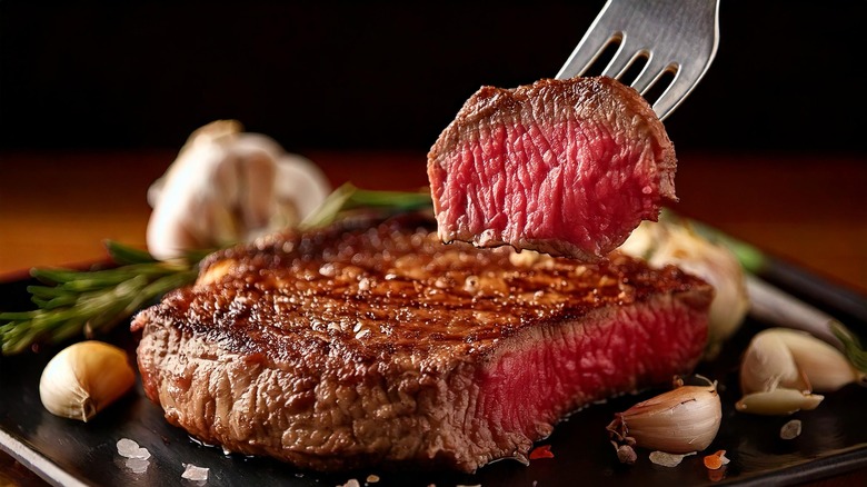 Medium rare steak partially sliced with a fork holding a piece of it