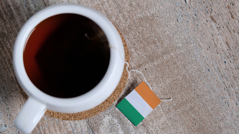 A cup of tea steeps, creating a robust and sightly reddish cup of tea, whose bag has an Irish flag