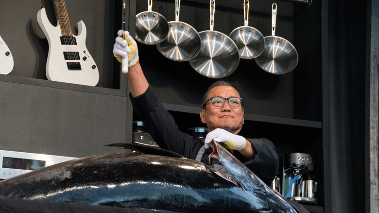 Chef Masaharu Morimoto holds a chef's knife over a fresh, whole tuna