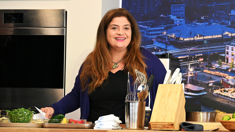 Chef Alex Guarnaschelli stands behind a wooden counter in a kitchen set