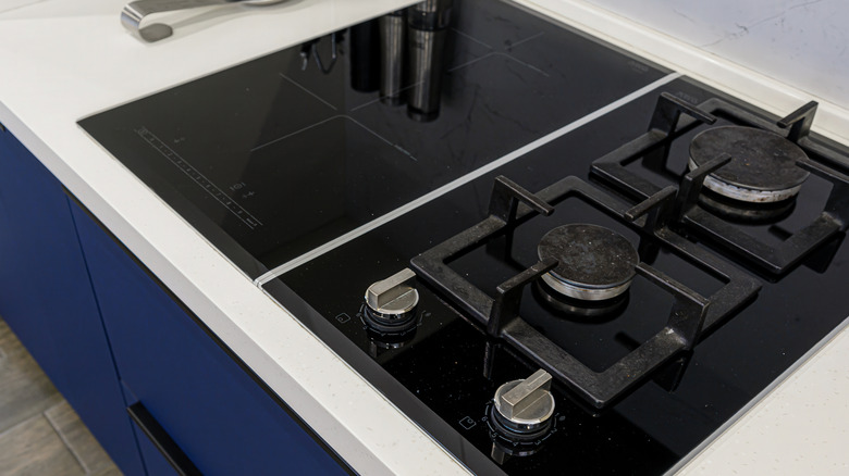 Close up of an induction and gas stove top set in white counter with blue cabinets