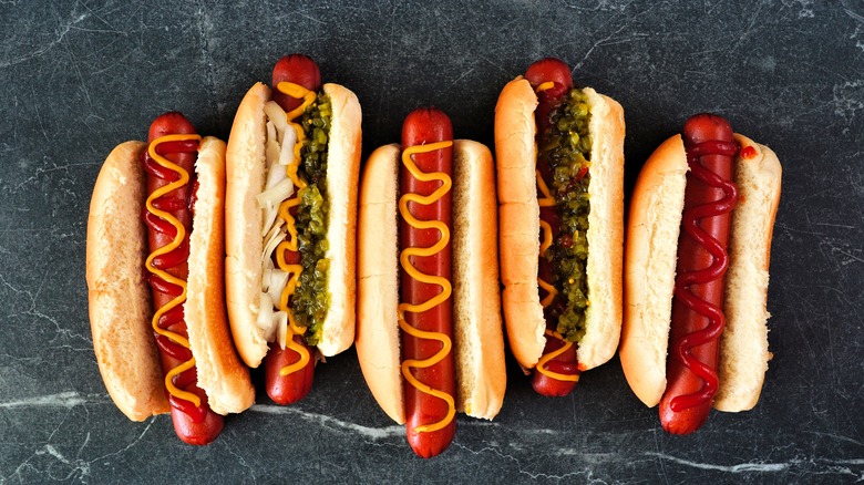 Five hot dogs with toppings on a slate background.