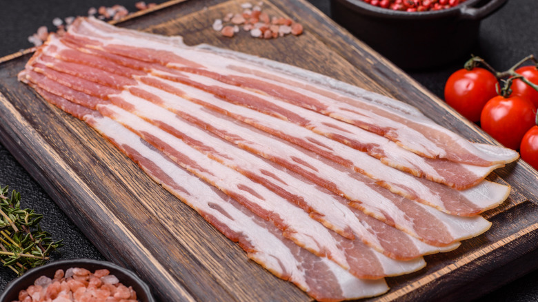 Raw strips of bacon on a wooden board.