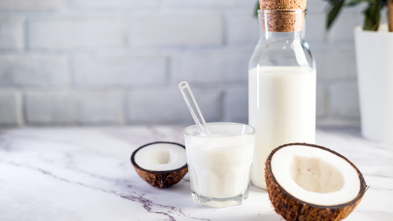 Glass of coconut milk, jar, and open fruit on white background